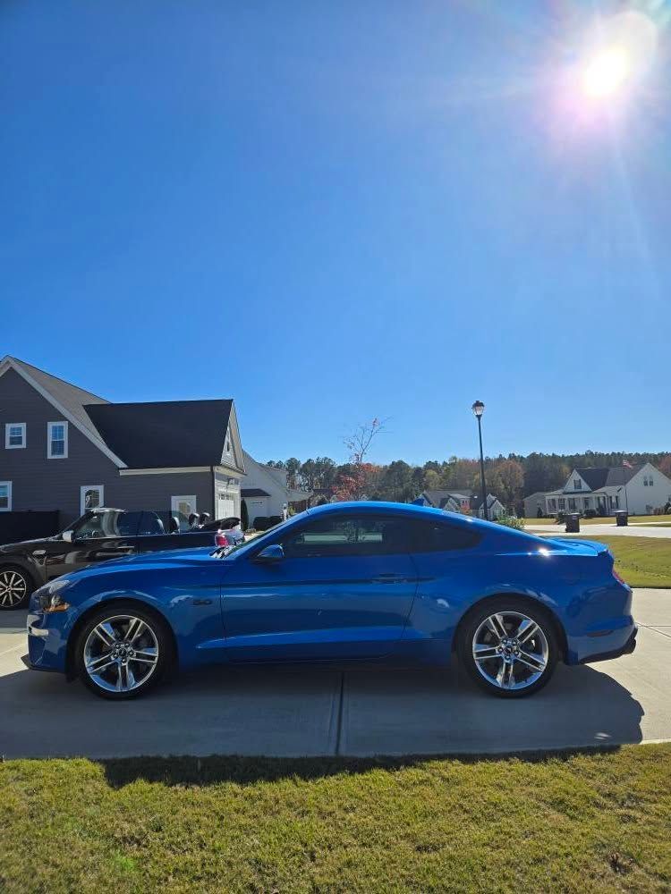 A blue mustang is parked in a driveway in front of a house.