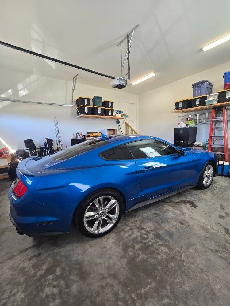 A blue mustang is parked in a garage under a garage door.