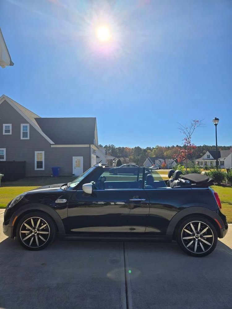 A black mini cooper convertible is parked in a driveway in front of a house.