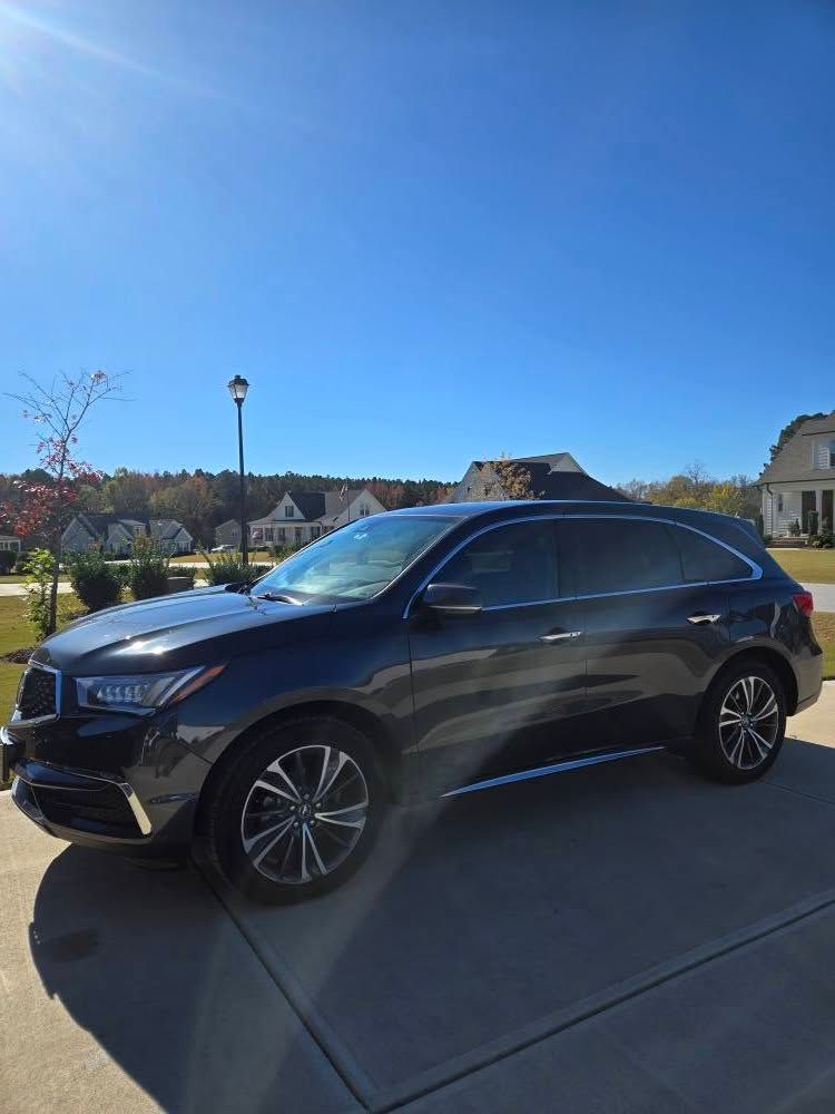 A black car is parked in a driveway on a sunny day.