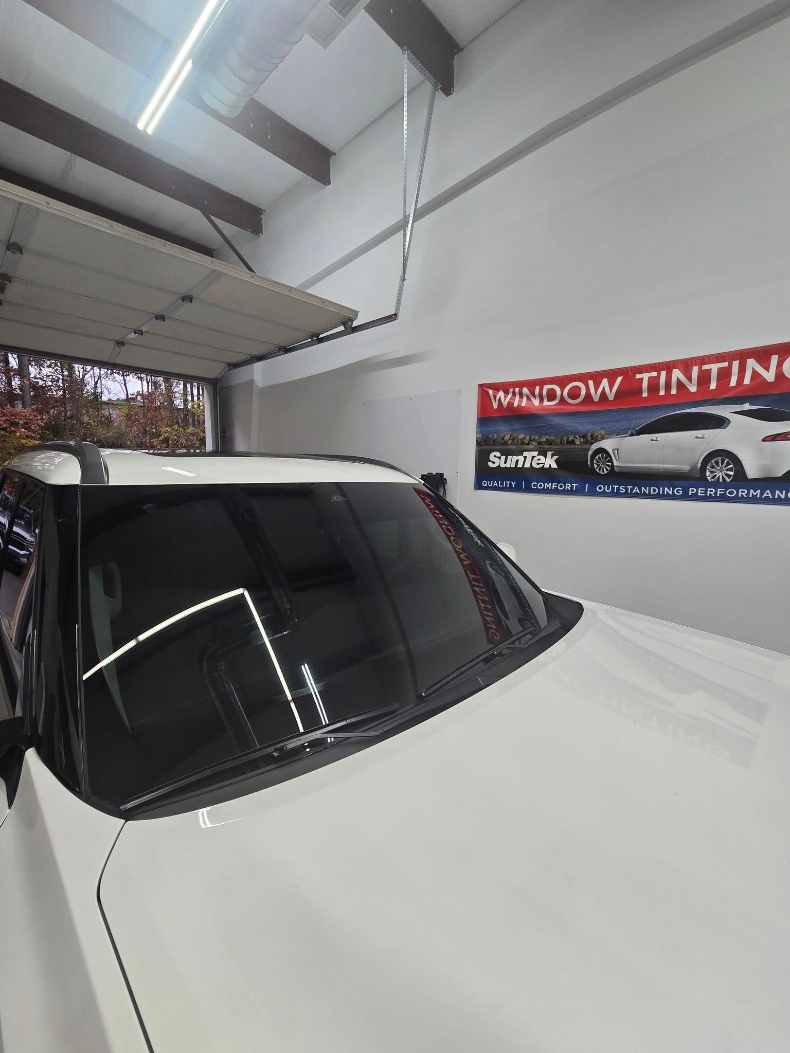 A white car is parked in a garage next to a window tinting sign.