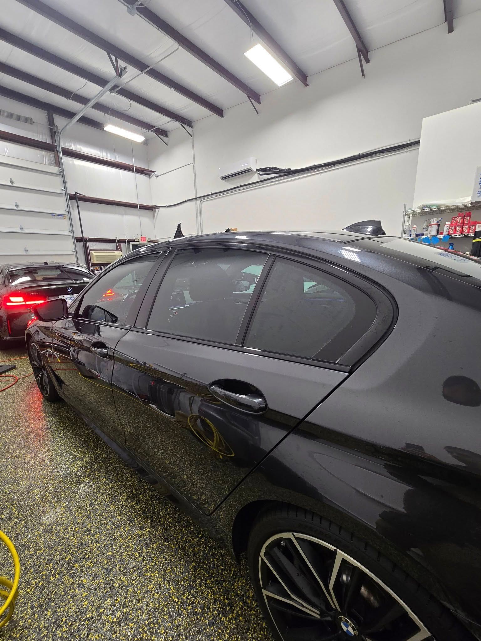 A black car is parked in a garage with a garage door open.