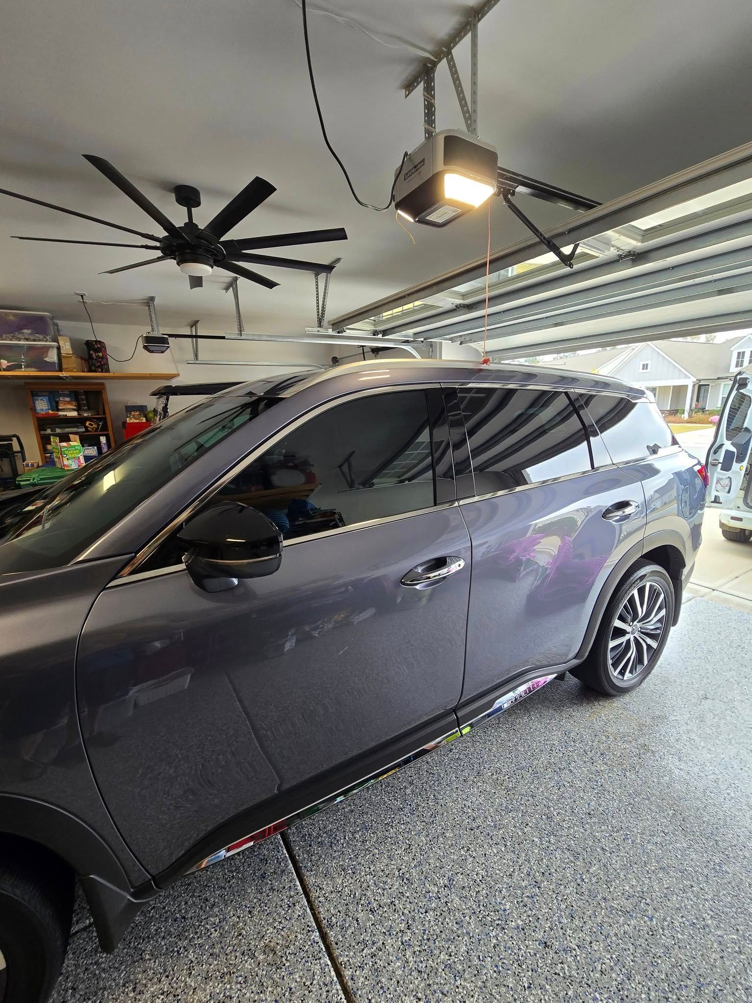 A car is parked in a garage under a ceiling fan.