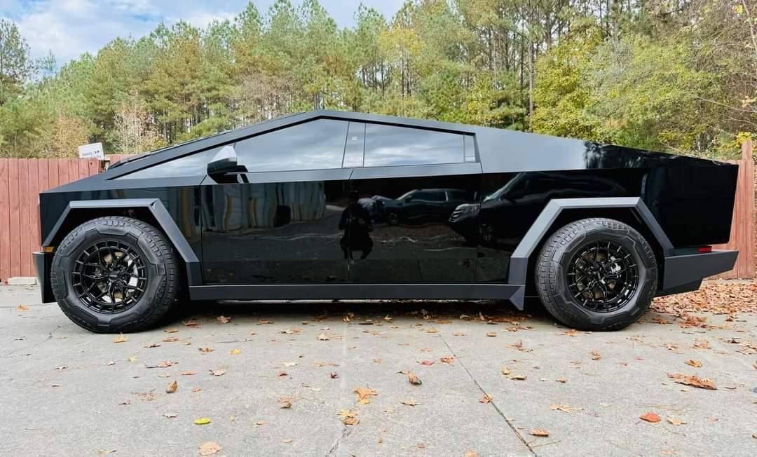 A black tesla cybertruck is parked in a driveway next to a wooden fence.
