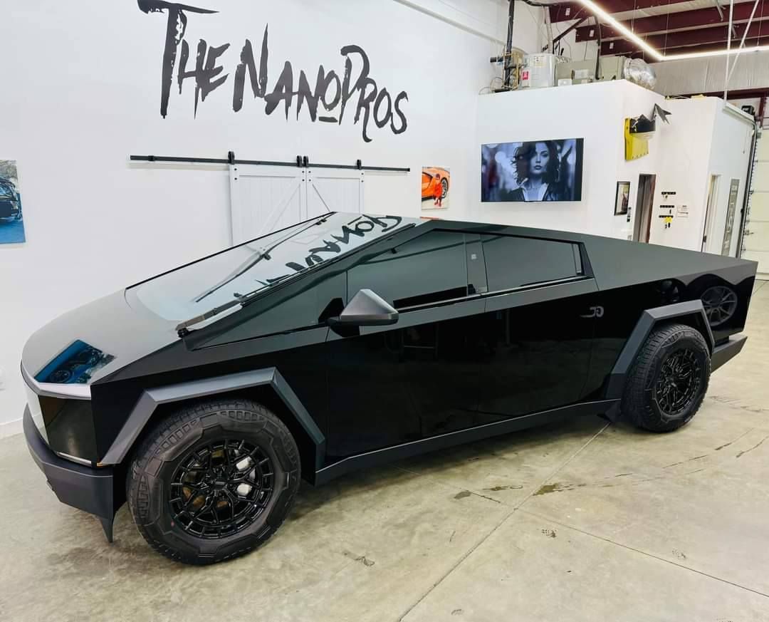 A black car is parked in front of a wall that says the nanopros