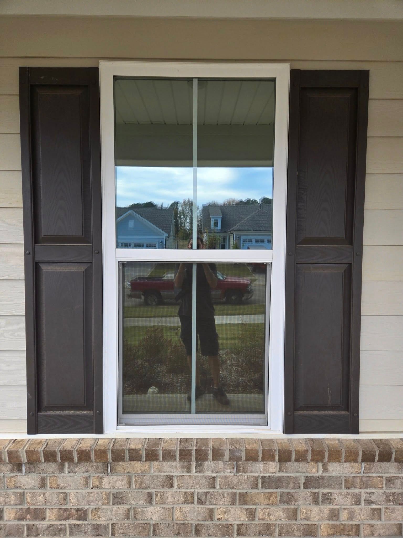 A white window with brown shutters on a brick house