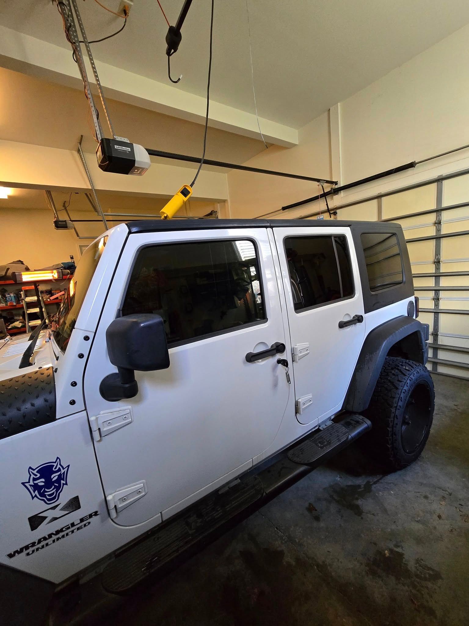 A white jeep is parked in a garage with a garage door opener.
