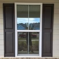 A white window with brown shutters on a house.