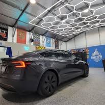 A tesla model s is parked in a garage with a honeycomb ceiling.