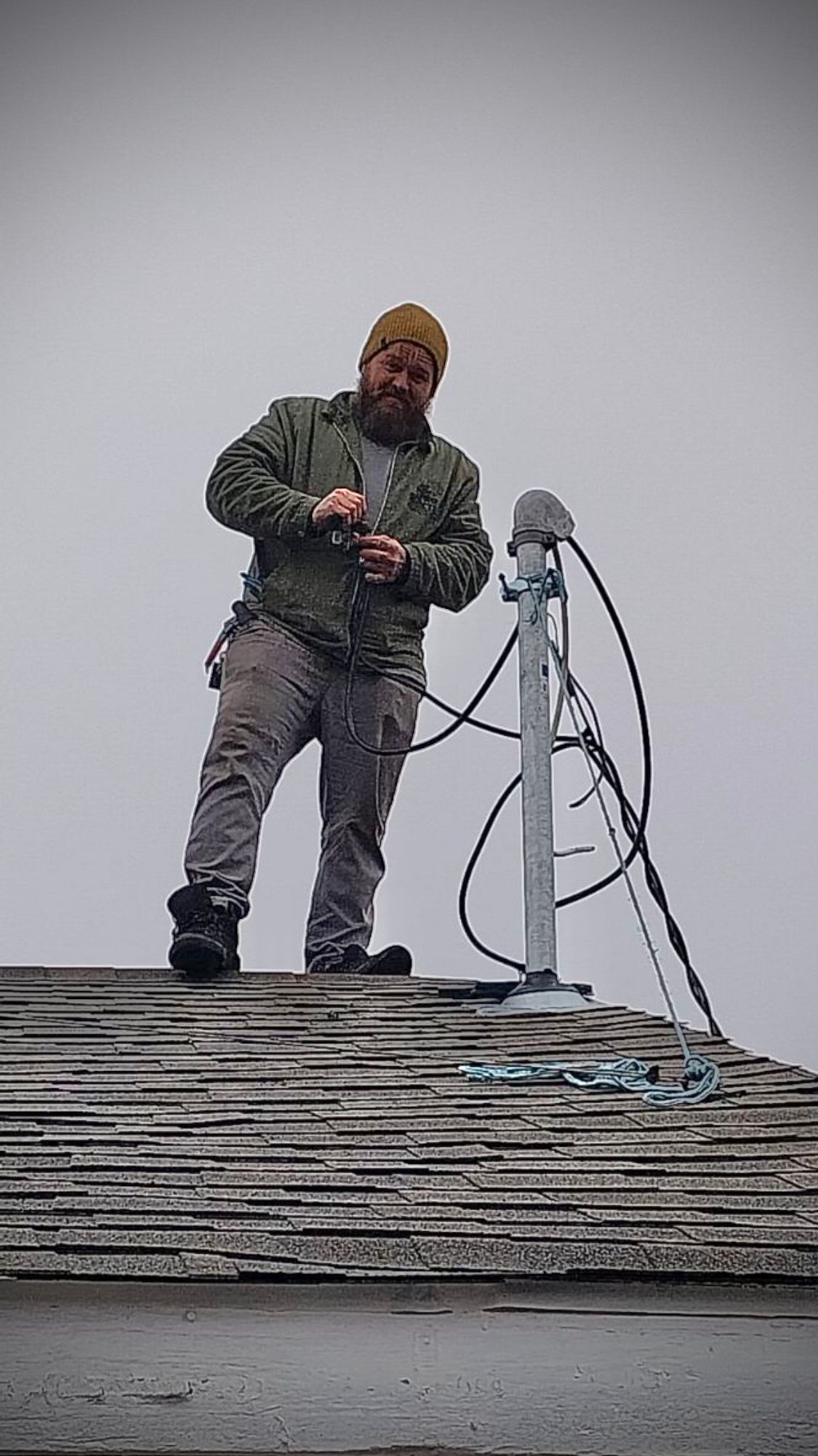 a man is standing on top of a roof working on a telephone pole