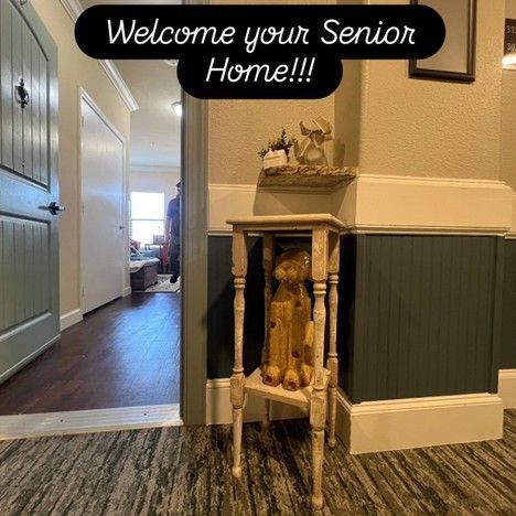 Hallway entrance with wooden side table and decorative items. Teal door and wainscotting. Text overlay: Welcome your Senior Home!!!