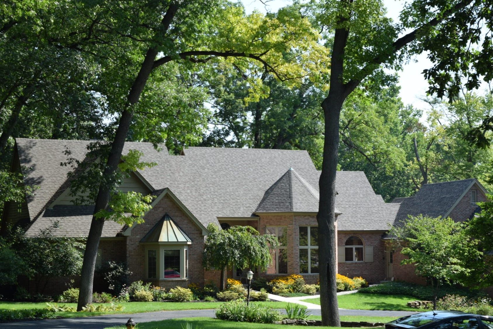 A brick house with a gray roof is surrounded by trees
