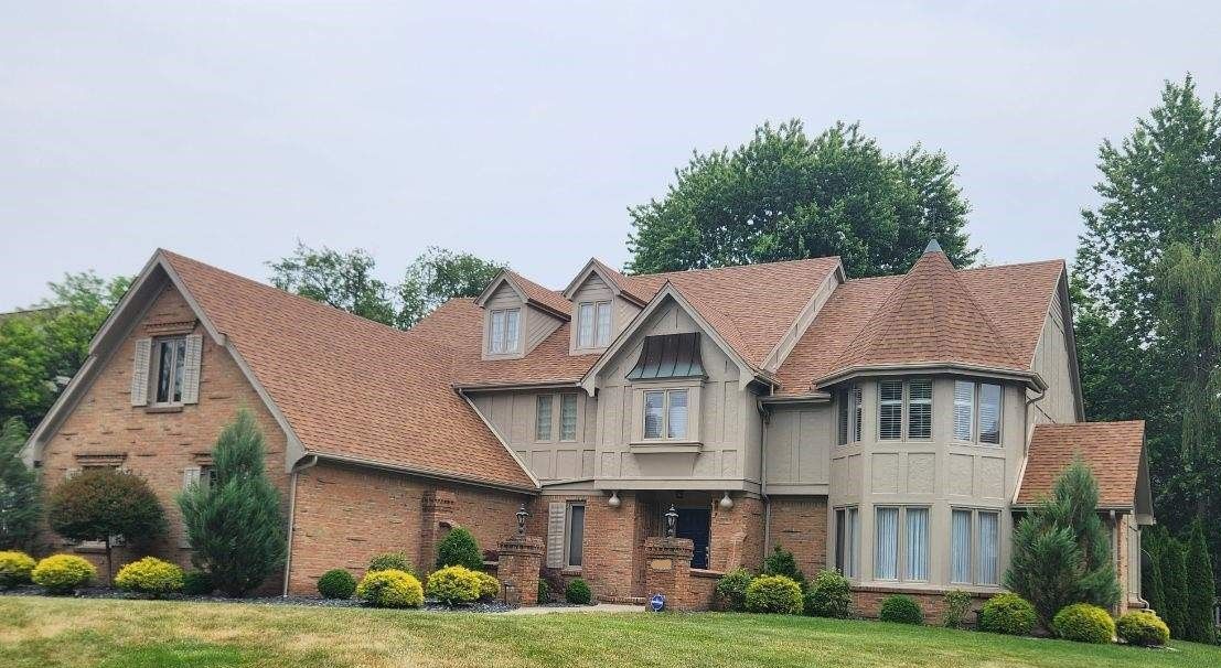 A large brick house with a brown roof is sitting on top of a grassy hill.