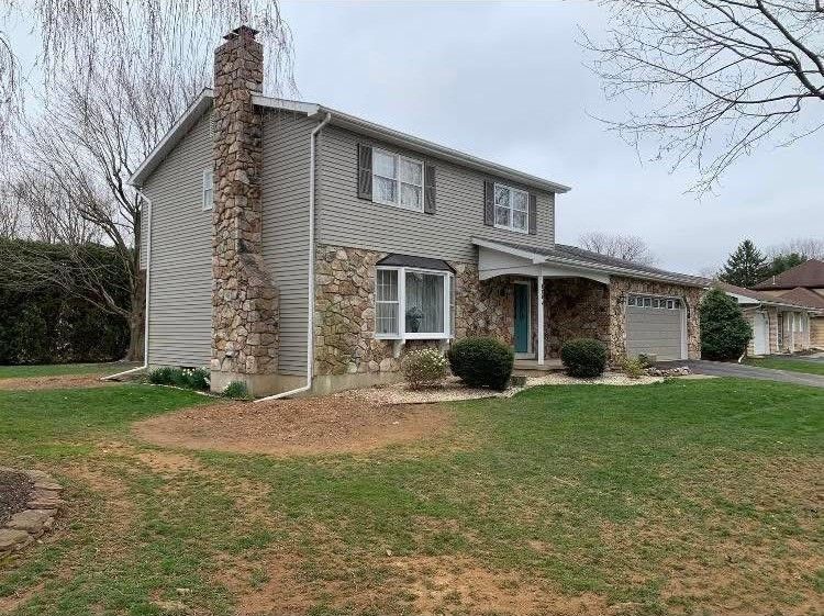 A large house with a stone chimney and a large lawn in front of it.
