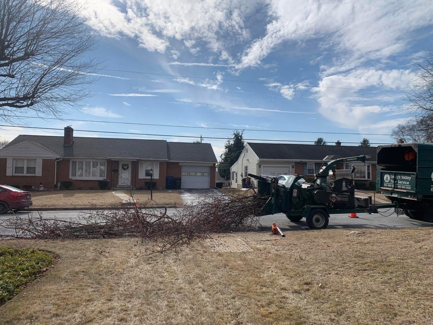 A tree chipper is cutting down a tree in front of a house.