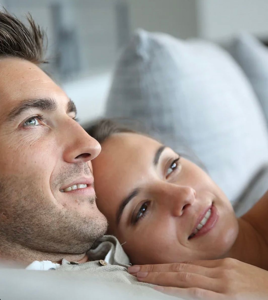 A man and a woman are laying on a couch and smiling.