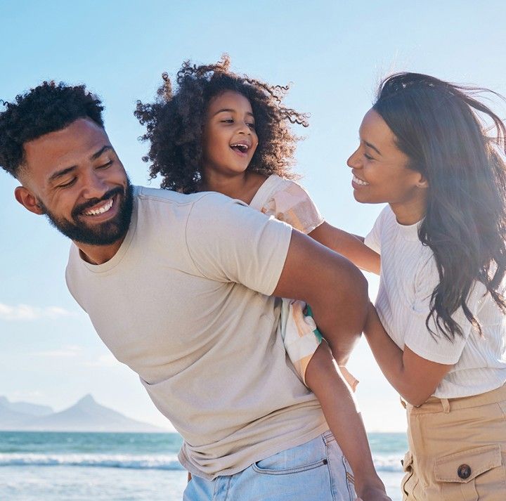 A man and woman are holding a little girl on the beach.