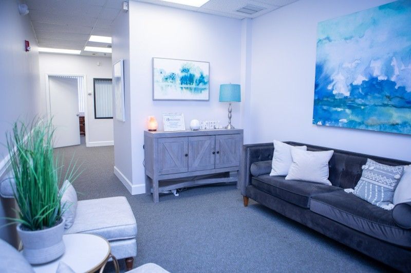 An office with a couch , chair , table and painting on the wall.
