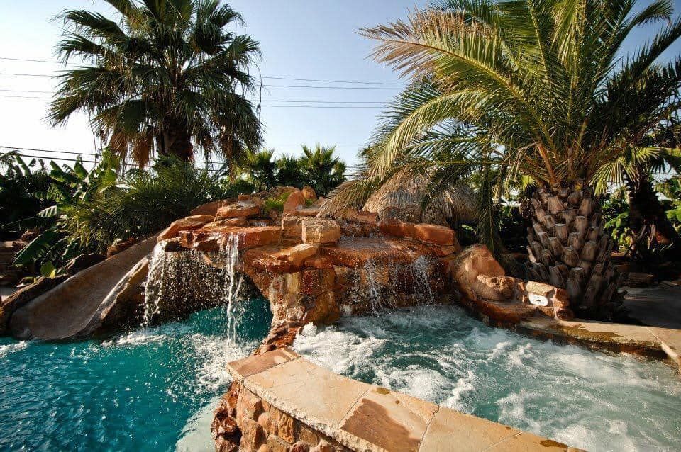 A large swimming pool surrounded by palm trees and a waterfall