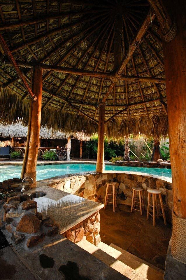 A gazebo with a thatched roof over a swimming pool.