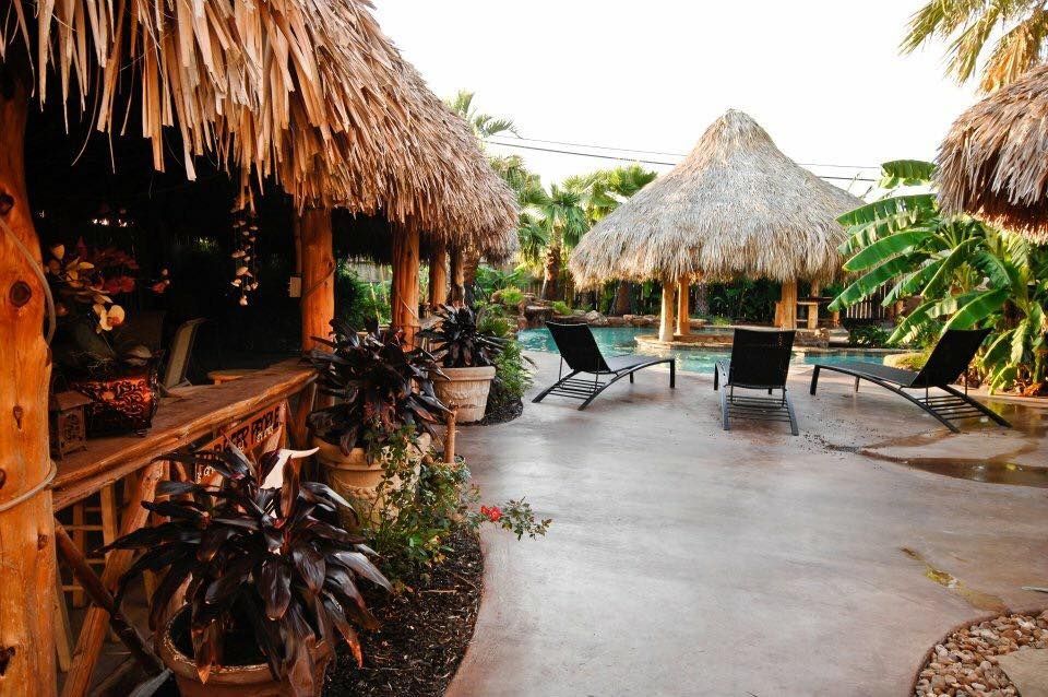 A patio with thatched roofs and chairs and a pool