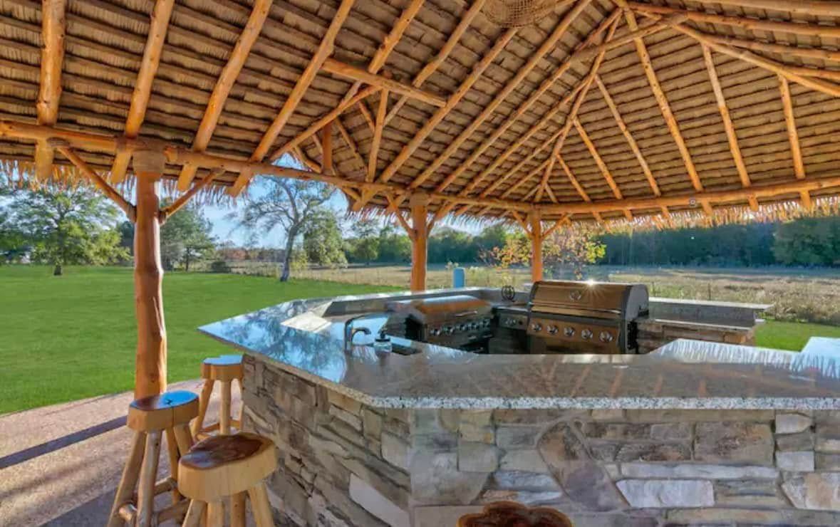 A gazebo with a grill and stools underneath it.