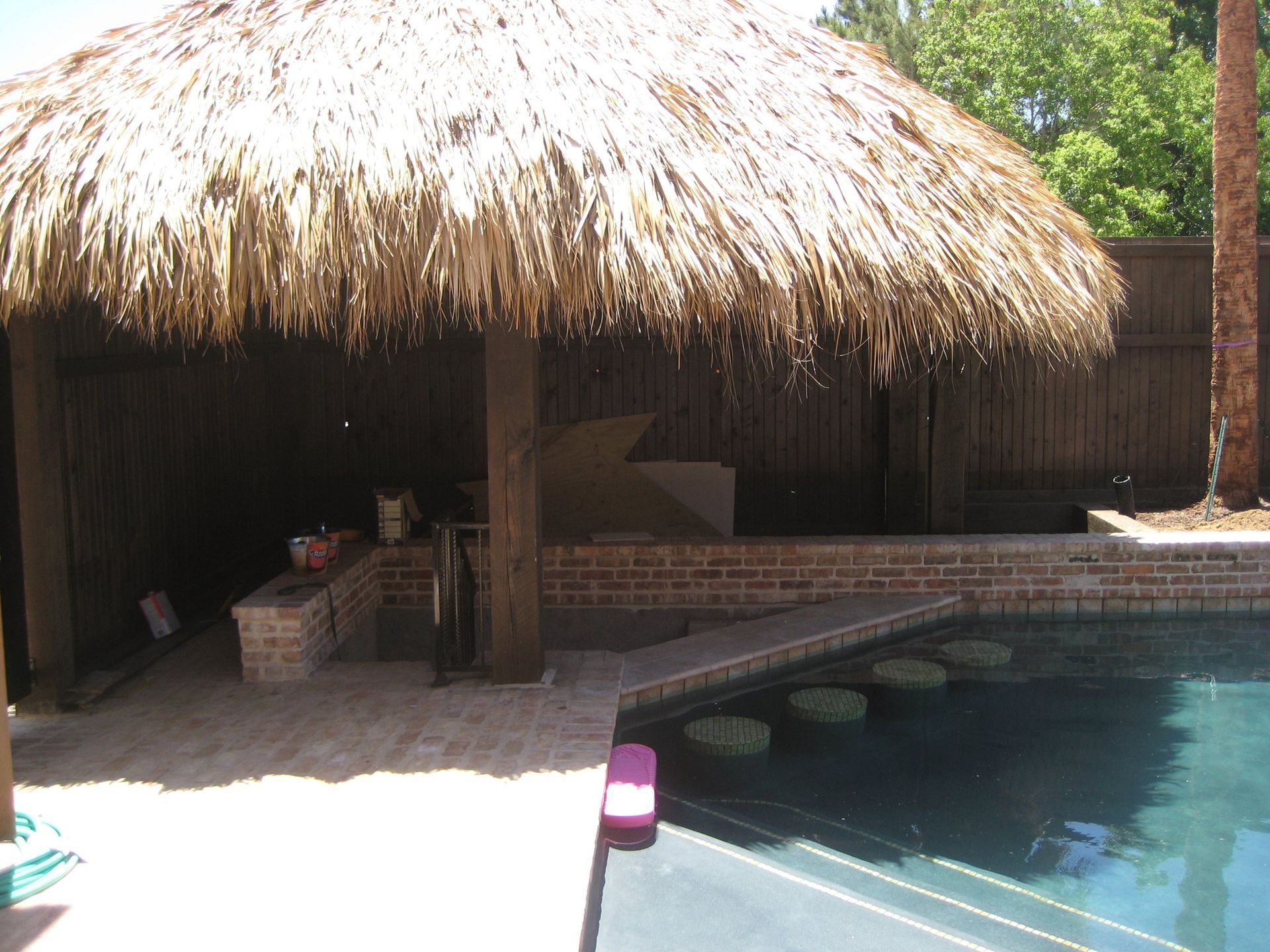 A pool with a thatched roof and a brick wall