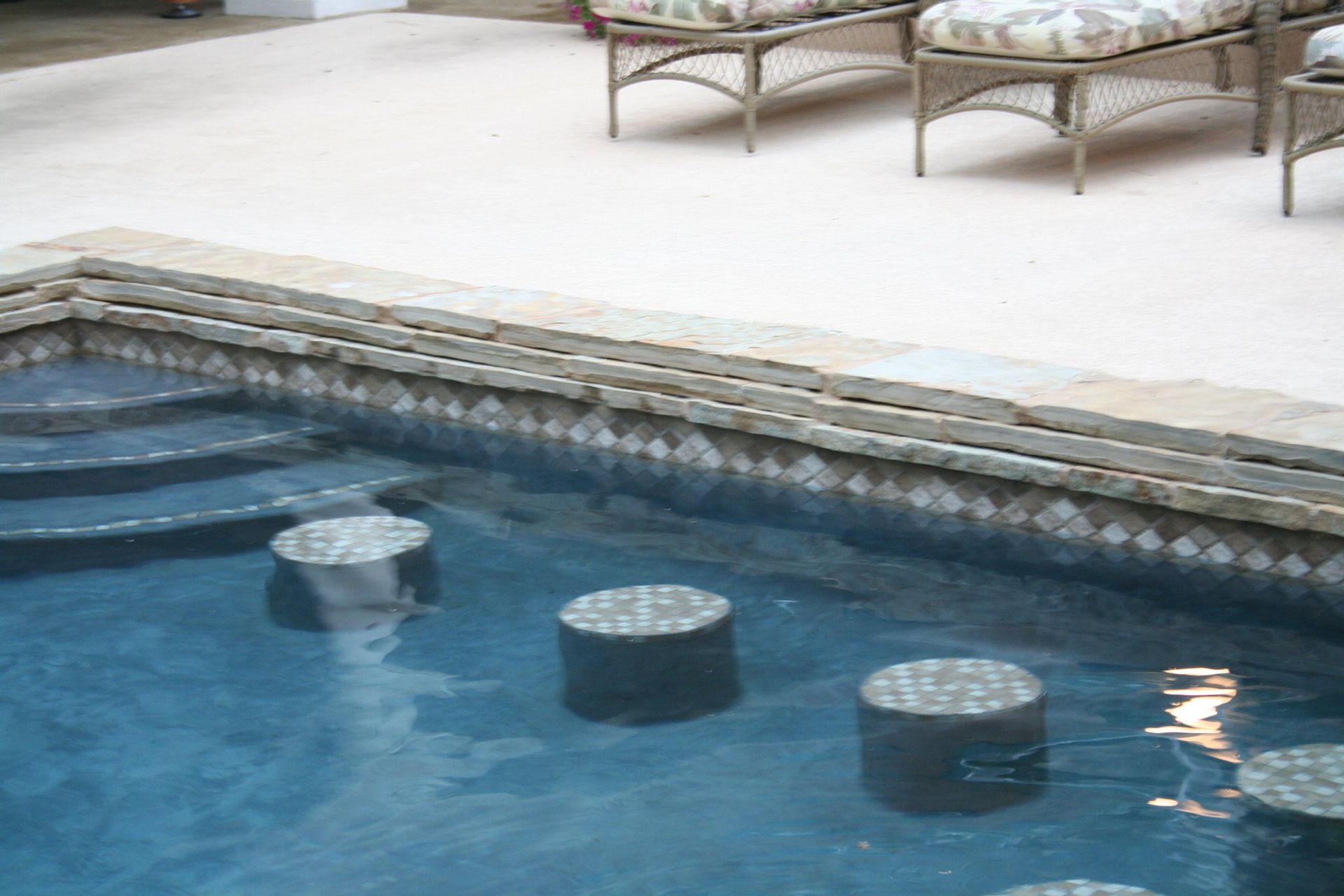 A swimming pool with chairs and ottomans around it