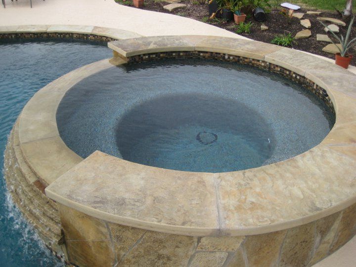 A hot tub surrounded by a stone wall next to a swimming pool
