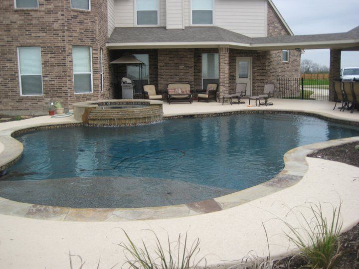 A large swimming pool in front of a brick house