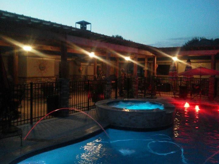 A large swimming pool is lit up at night with a fountain in the middle.