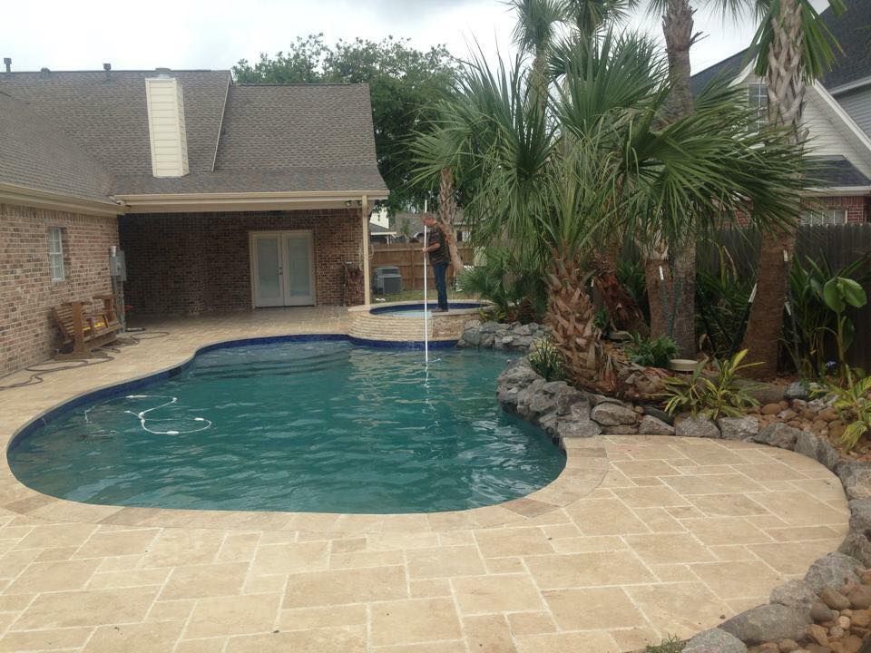 A large swimming pool is in the backyard of a house surrounded by palm trees.