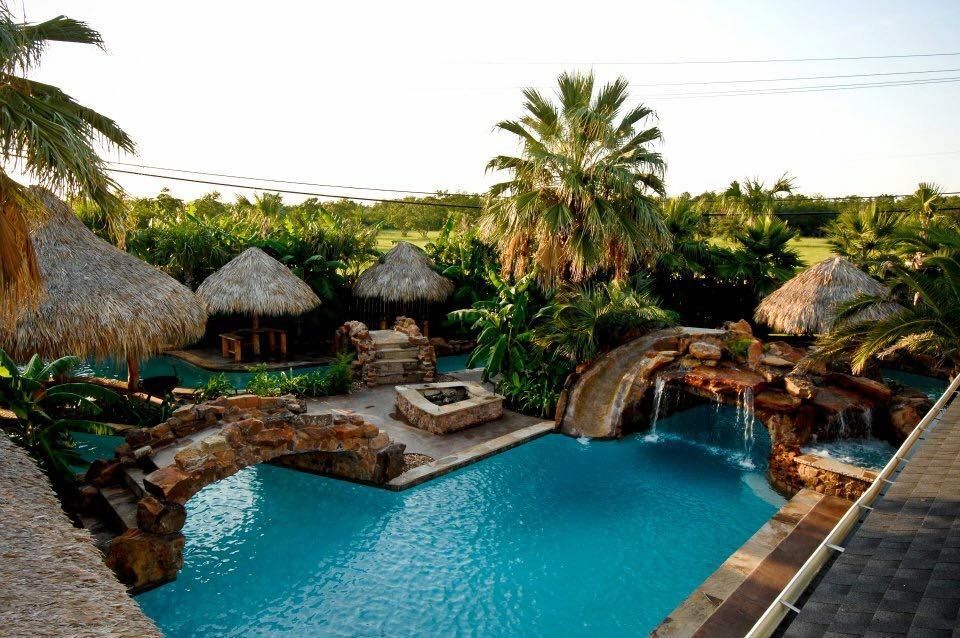 A large swimming pool surrounded by palm trees and thatched roofs