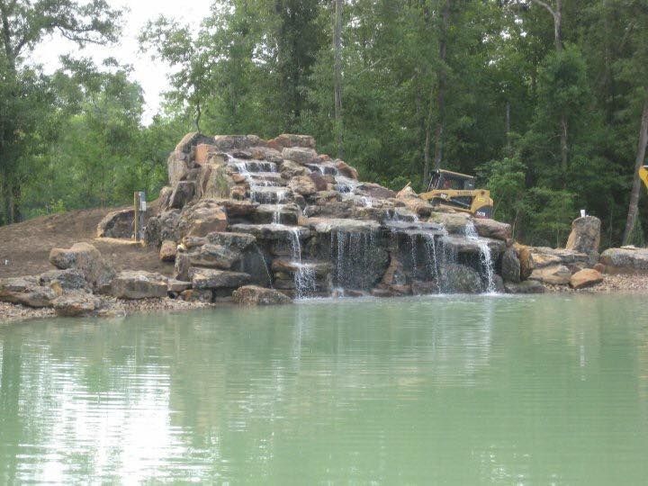 There is a waterfall in the middle of a pond surrounded by trees.