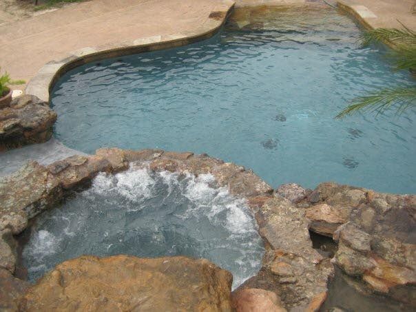 A large swimming pool surrounded by rocks and a hot tub.