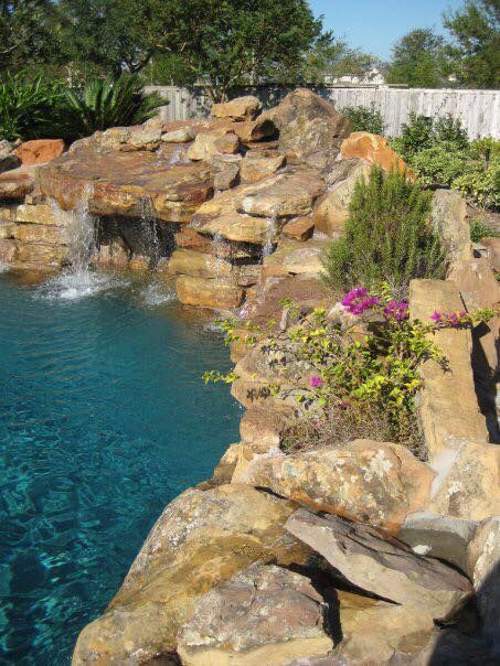 A swimming pool with a waterfall surrounded by rocks and flowers