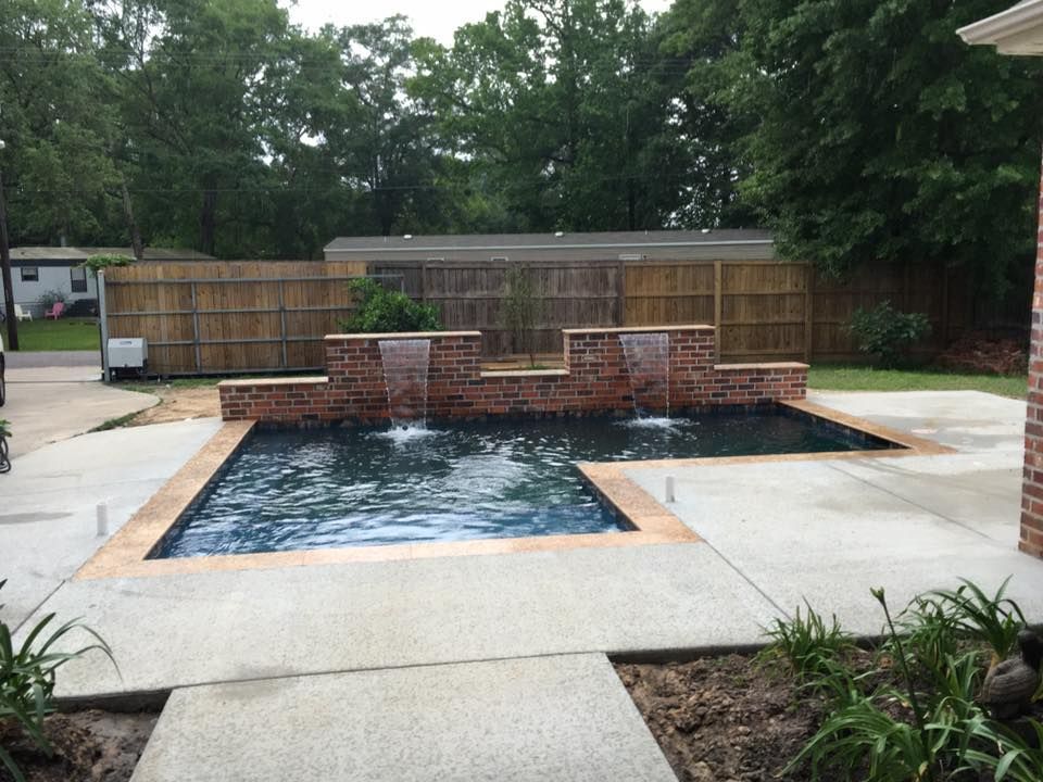 A large swimming pool with a waterfall in the backyard of a house.