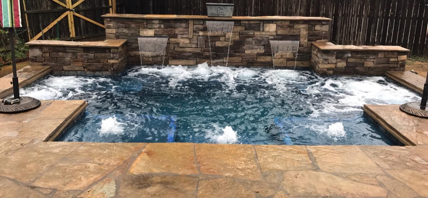 A large swimming pool with a waterfall in the backyard.