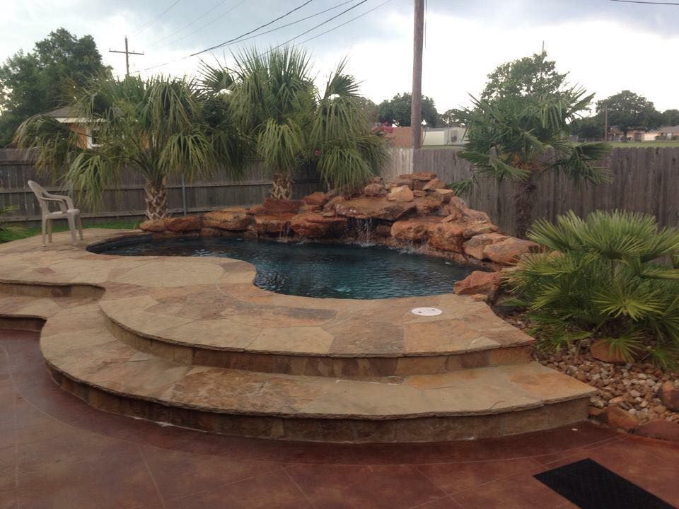A swimming pool with steps and a waterfall in the backyard