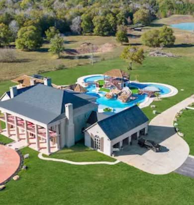 An aerial view of a large house with a pool in the middle of a lush green field.