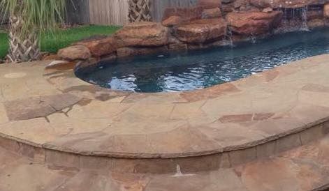 A large swimming pool with a waterfall in the backyard.