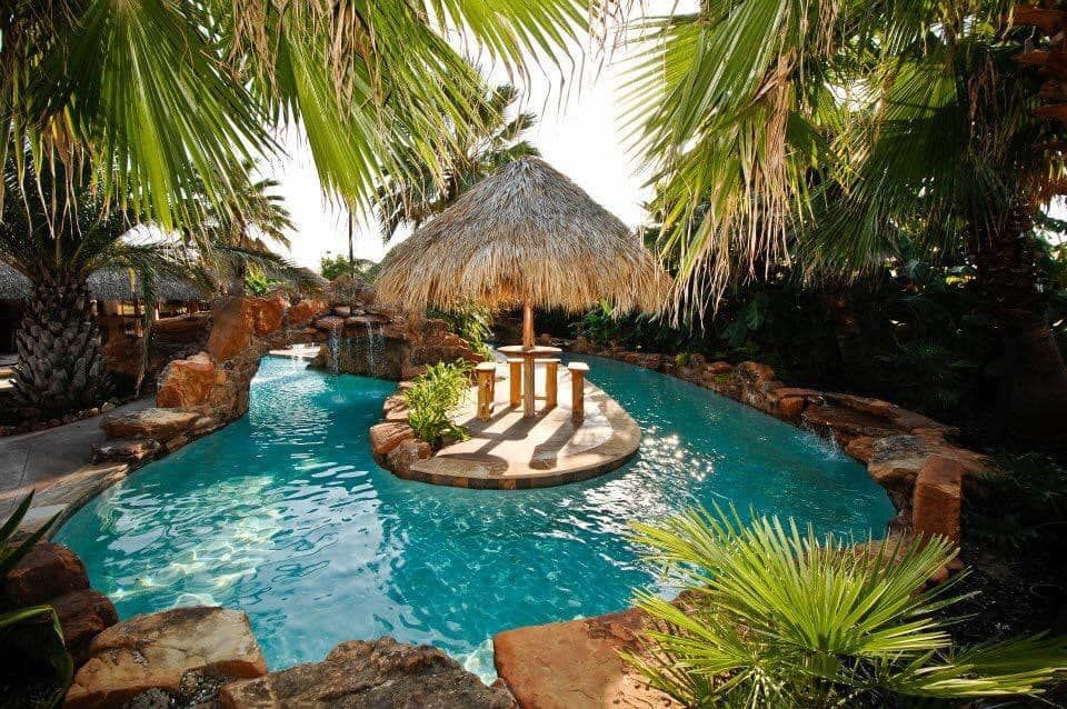 A large swimming pool surrounded by palm trees and a thatched hut
