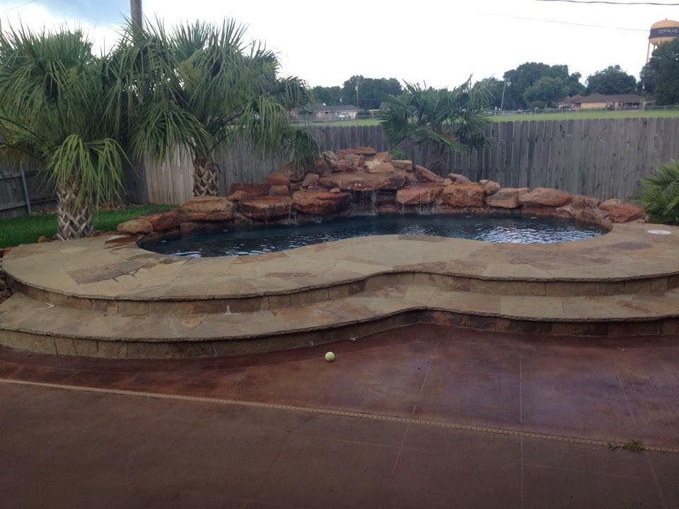 A swimming pool with steps and a waterfall in the backyard of a house.