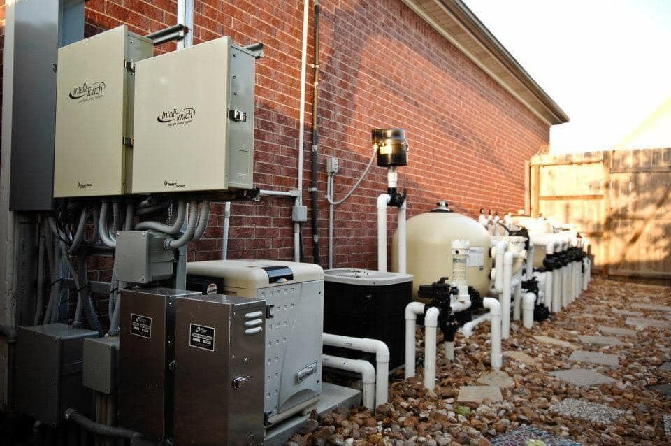A row of swimming pool equipment is sitting outside of a brick building.