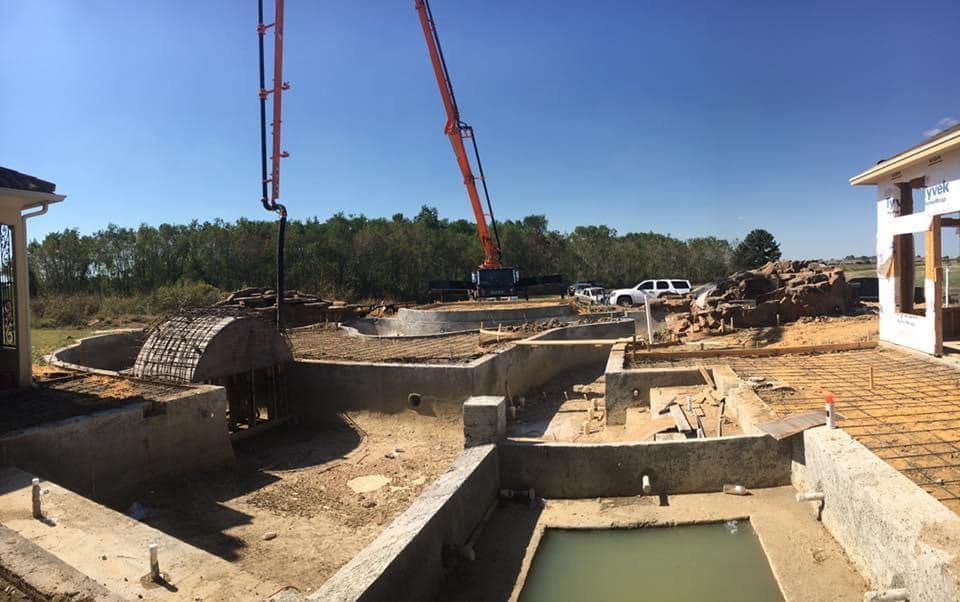 A large crane is being used to pour concrete into a pool.
