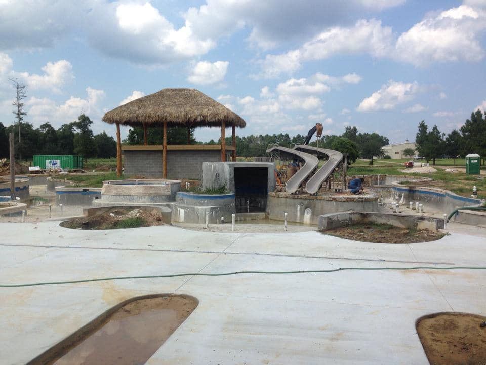 A swimming pool under construction with a thatched hut in the background