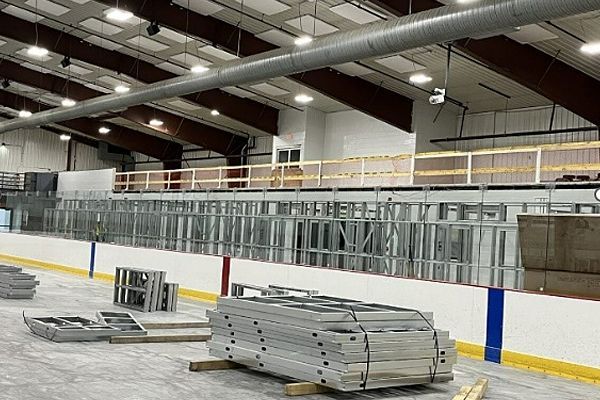 A stack of ladders is sitting on the ice rink in a building under construction.