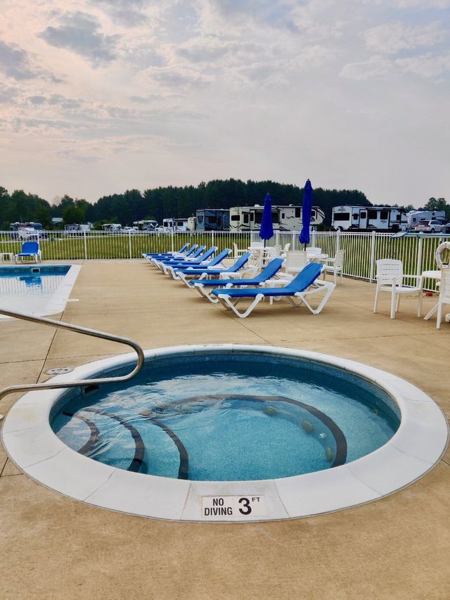 a hot tub is surrounded by chairs and umbrellas next to a swimming pool .