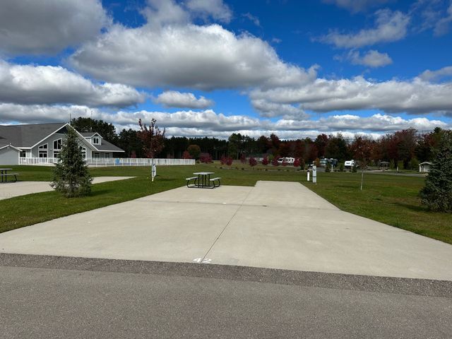 a concrete driveway leading to a grassy field with a house in the background