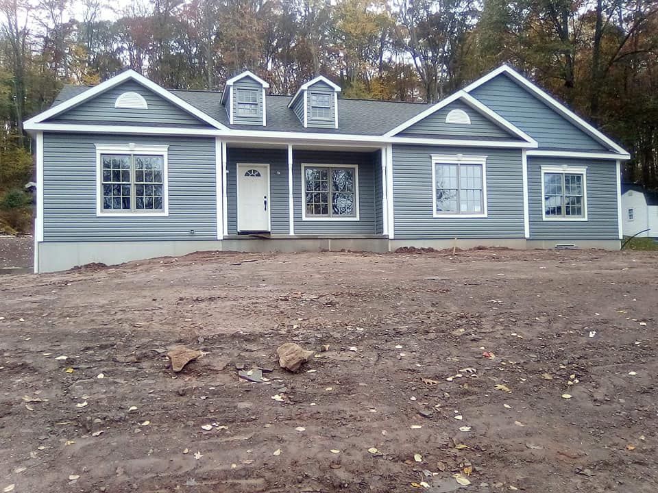 A gray house with white trim sits in a dirt field
